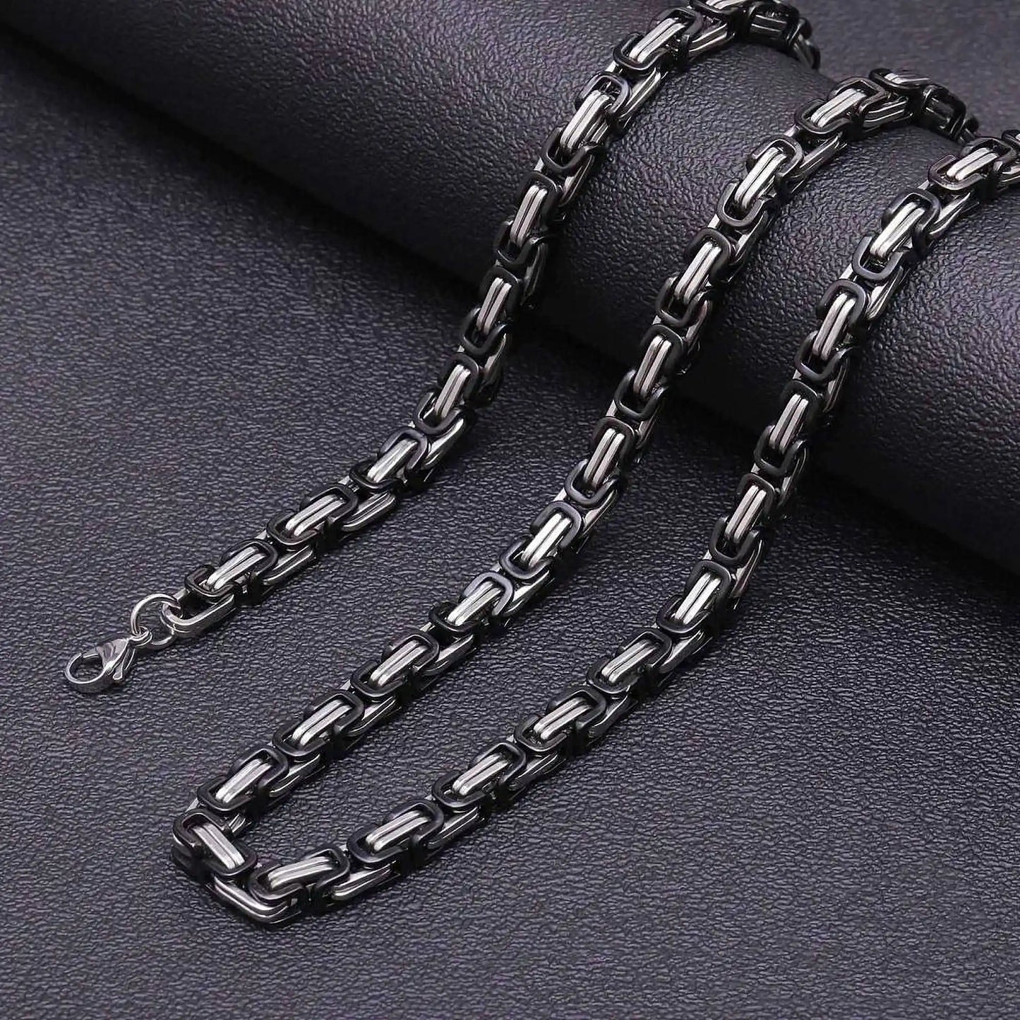 Black and silver byzantine chain necklace on a dark textured surface