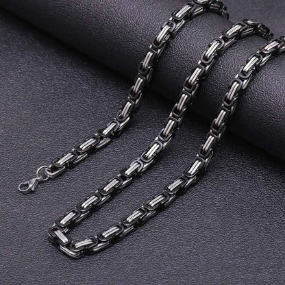 Black and silver byzantine chain necklace on a dark textured surface